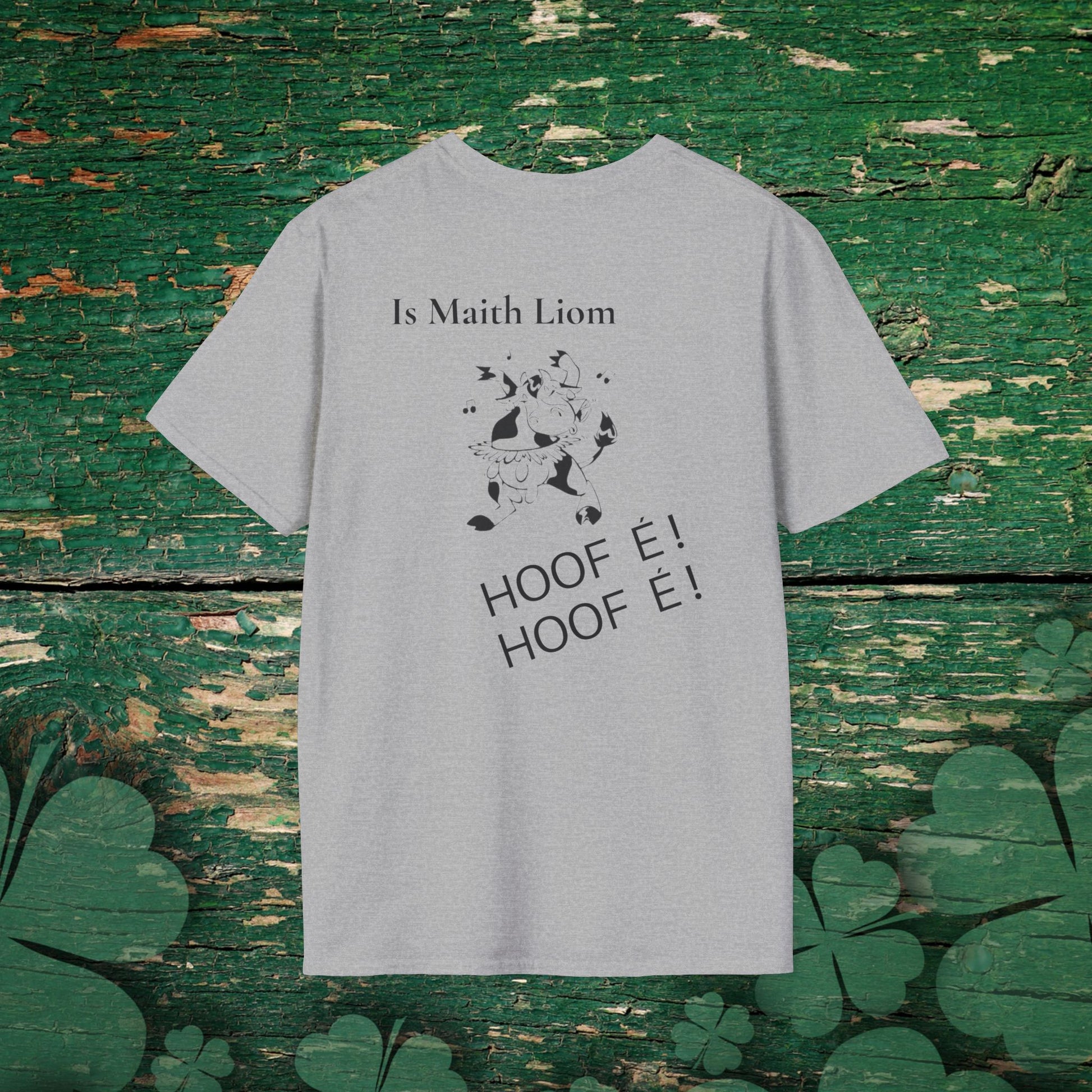 Unisex Grey t-shirt with Gaeilge phrase “Is Maith Liom HOOF É” and dancing cow illustration, playful heritage humor design on a green, distressed fence